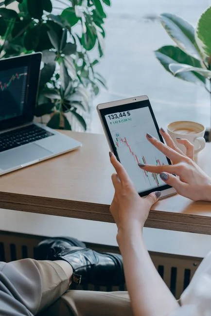 Two businessmen examine stock market data with a smartphone and laptop in a modern office setting.
